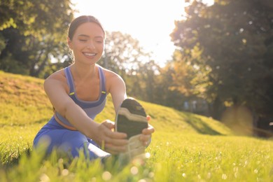 Photo of Attractive woman doing exercises on green grass in park, space for text. Stretching outdoors
