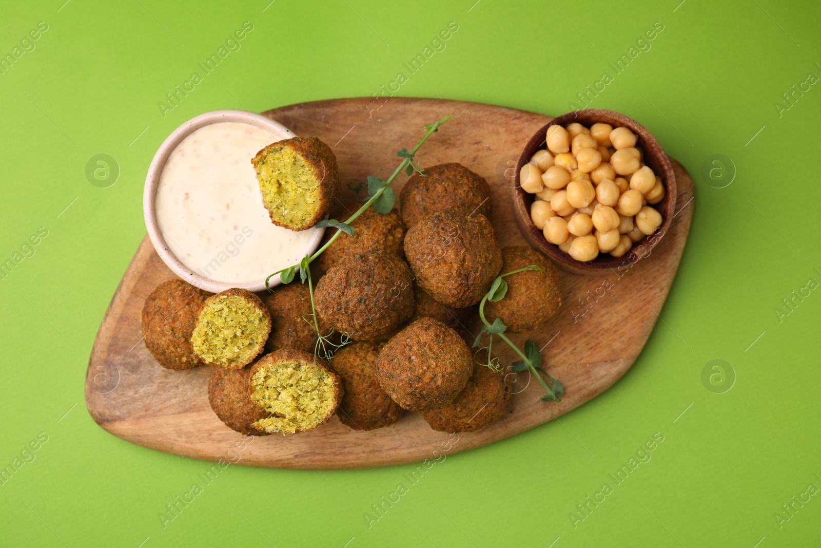 Photo of Delicious falafel balls, chickpeas and sauce on green background, top view