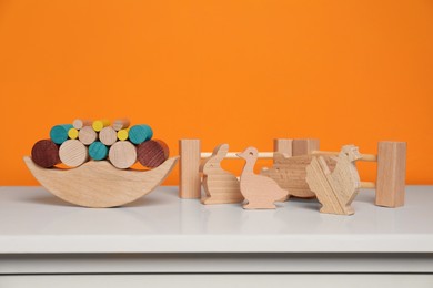 Photo of Wooden balance toy, animals and fence on white chest of drawers near orange wall, space for text. Children's development