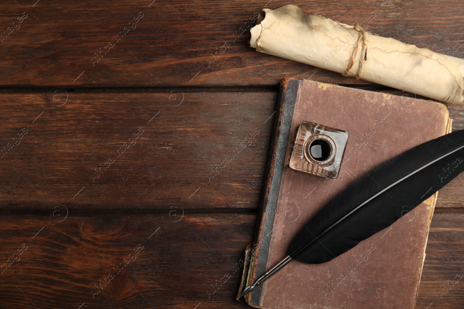 Photo of Feather pen, inkwell, old book and parchment scroll on wooden table, flat lay. Space for text