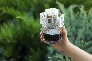 Photo of Woman holding glass with drip coffee bag outdoors, closeup