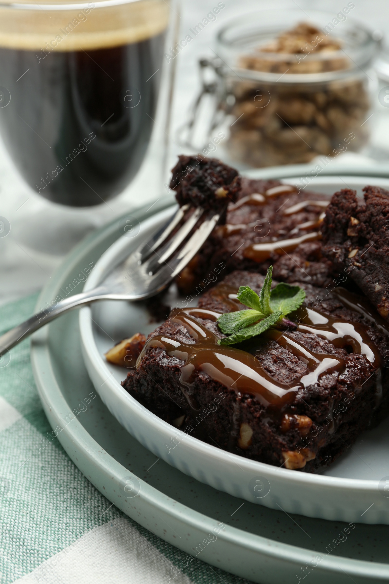 Photo of Delicious chocolate brownies with nuts, caramel sauce and fresh mint on napkin, closeup