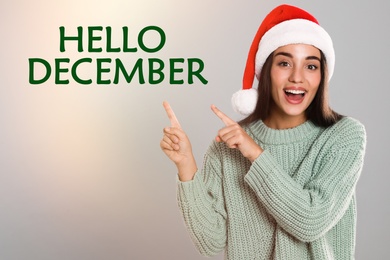 Image of Hello December greeting card. Happy woman in Santa hat on light background