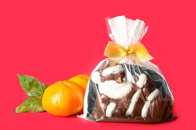 Photo of Chocolate Santa Claus candy and tangerines on red background