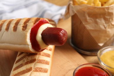 Delicious french hot dog, fries and dip sauces on wooden table, closeup