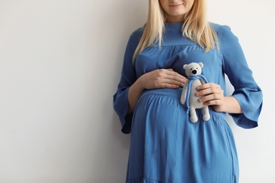 Photo of Pregnant woman holding toy near tummy on light background, closeup. Space for text