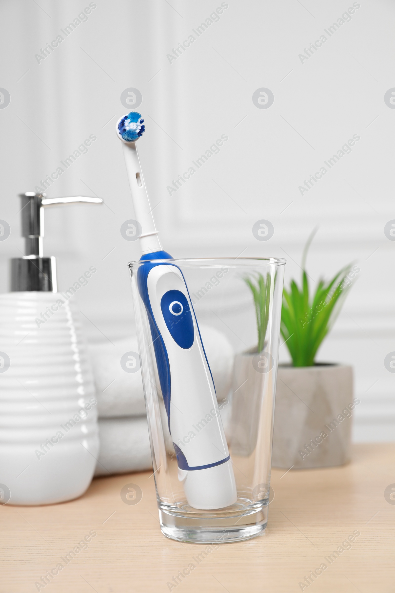 Photo of Electric toothbrush, soap dispenser and towels on wooden table