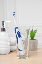 Photo of Electric toothbrush, soap dispenser and towels on wooden table
