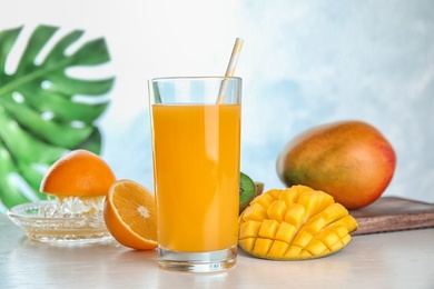 Photo of Glass of fresh mango drink and tropical fruits on table against color background