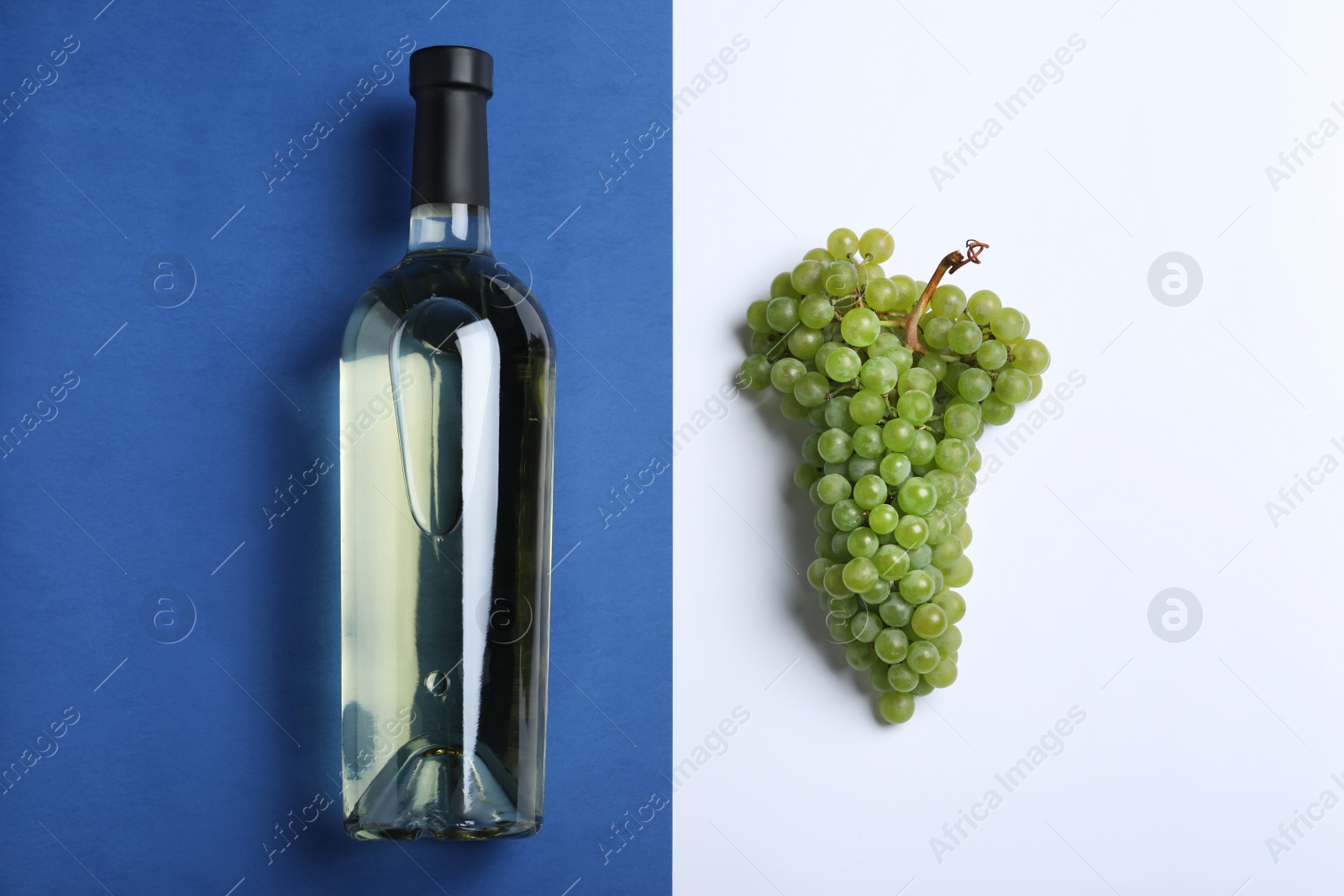 Photo of Fresh ripe juicy grapes and bottle of wine on color background, flat lay