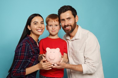 Photo of Happy family with ceramic piggy bank on light blue background