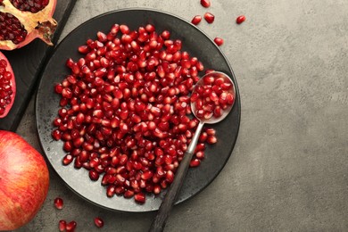 Photo of Ripe juicy pomegranate grains on grey textured table, flat lay. Space for text