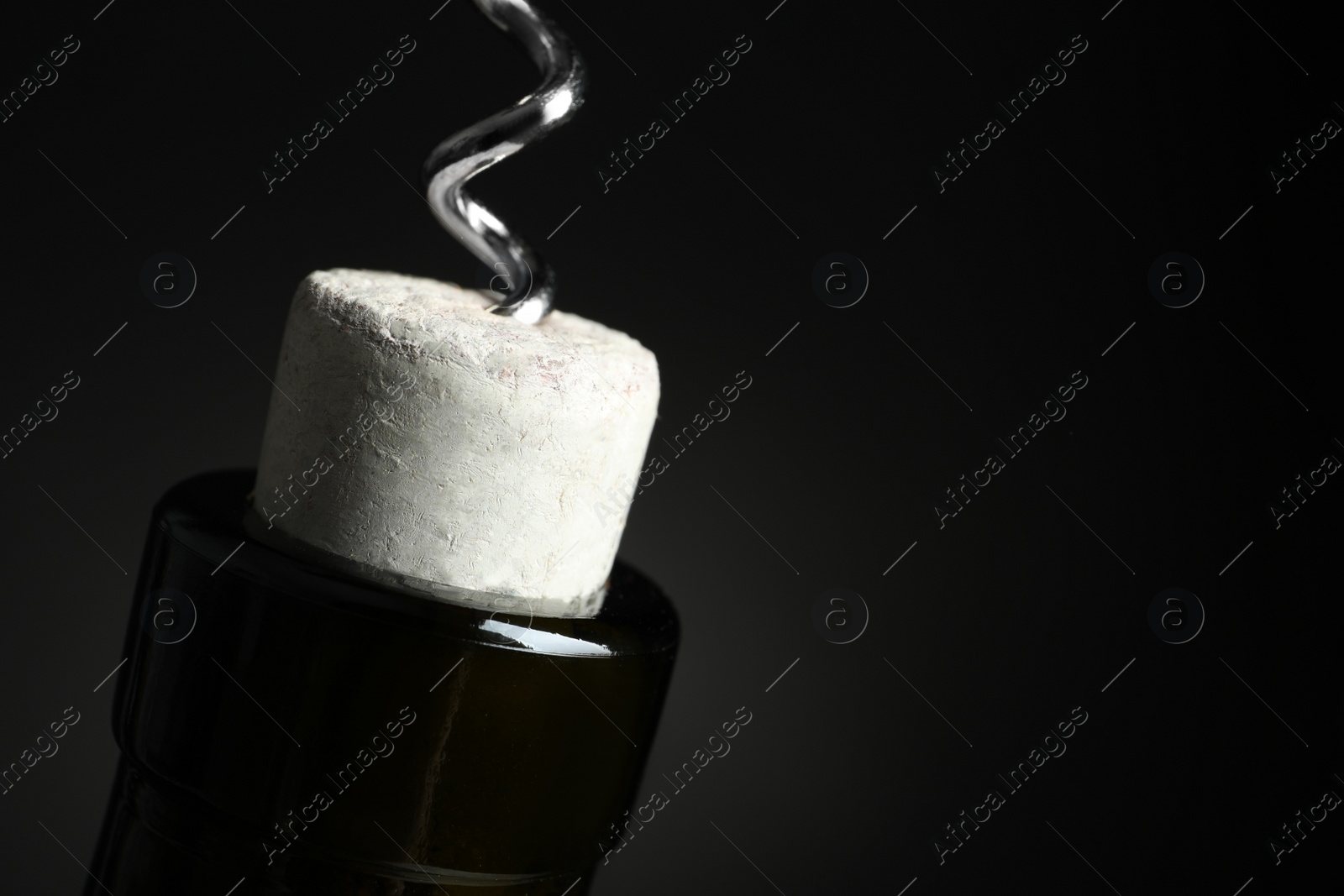 Photo of Opening bottle of wine with corkscrew on dark background, closeup