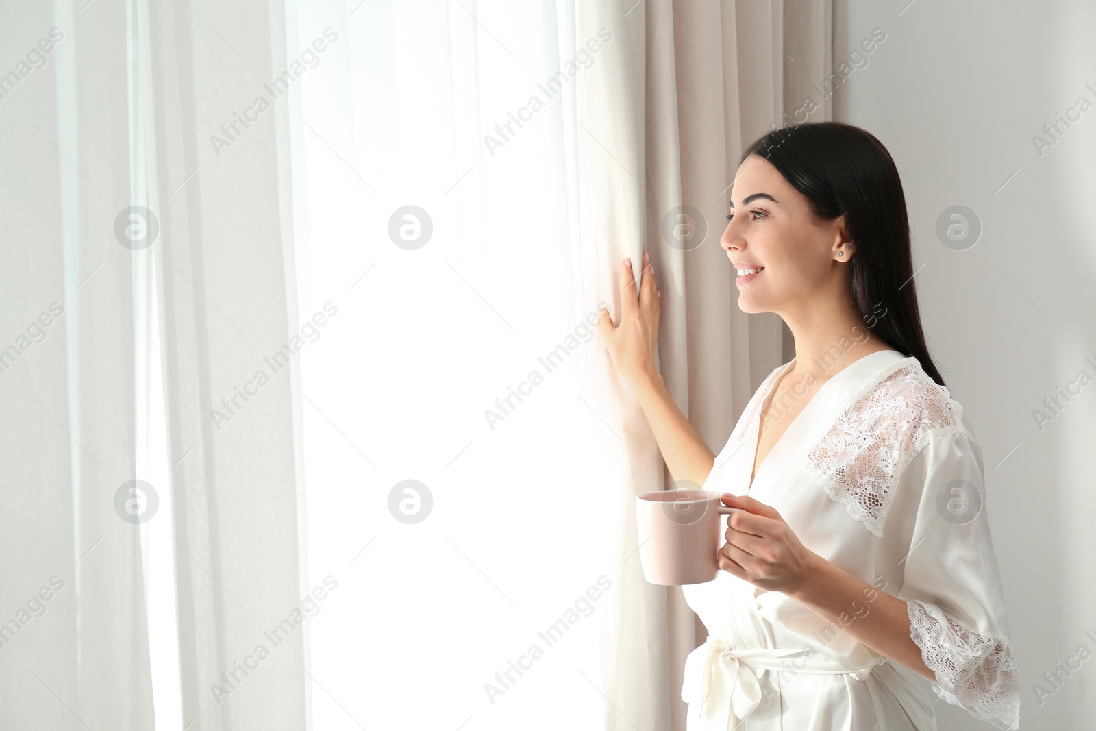Photo of Young woman with cup of coffee near window. Lazy morning