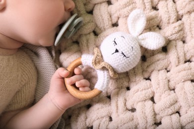 Cute newborn baby with pacifier and toy bunny on beige crocheted plaid, top view