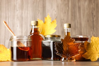 Photo of Bottles and jars of tasty maple syrup on wooden table