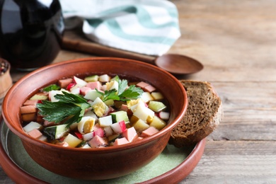 Photo of Delicious cold okroshka with kvass served on wooden table, closeup. Traditional Russian summer soup