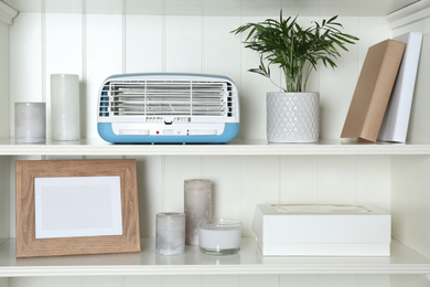 Photo of Modern air purifier and different items on white wooden shelves