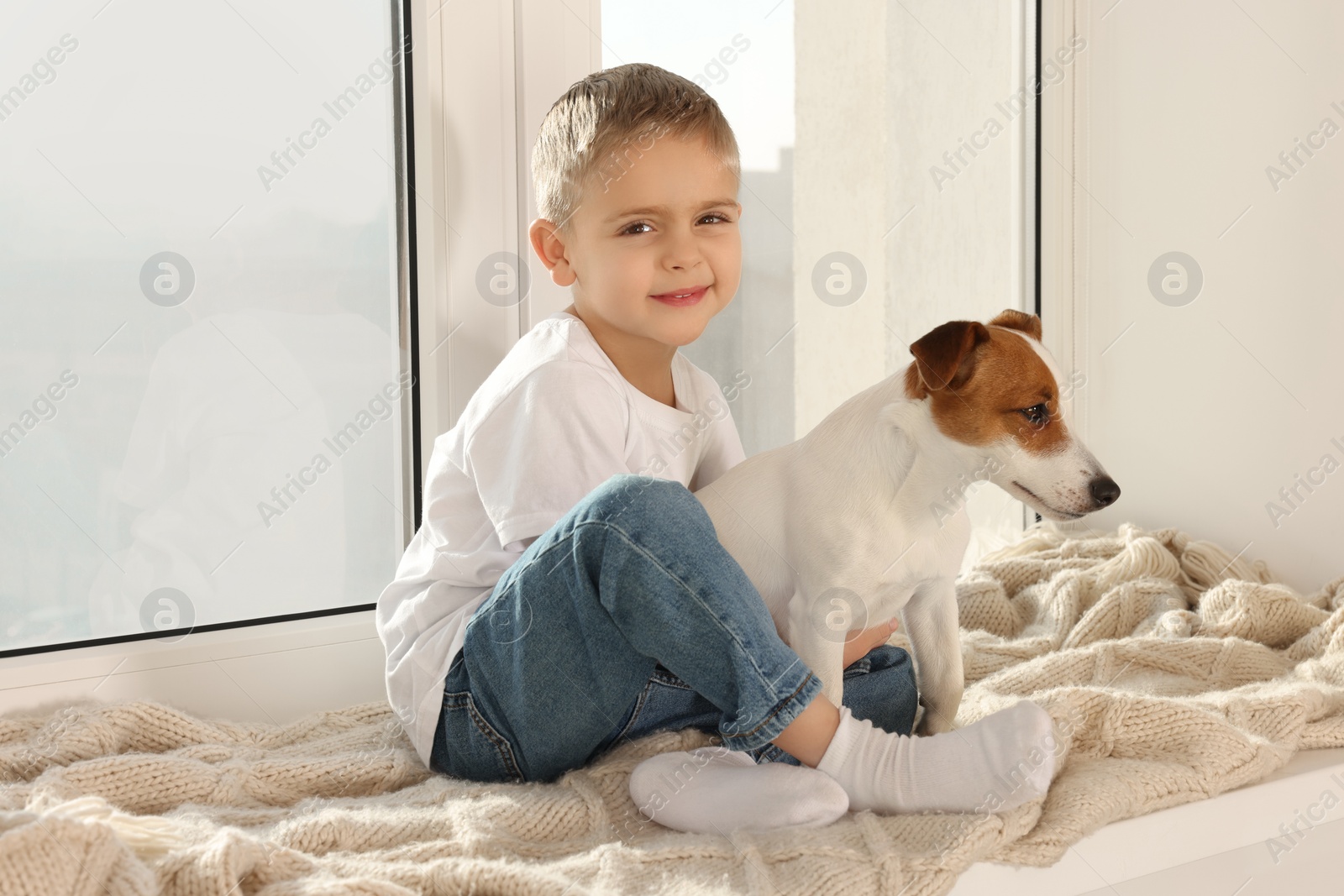 Photo of Little boy with his cute dog on windowsill at home. Adorable pet