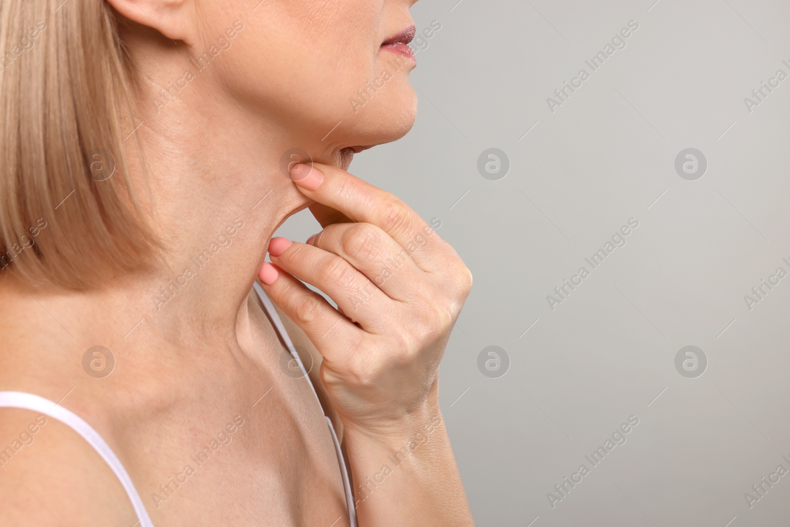 Photo of Woman touching her neck on grey background, closeup