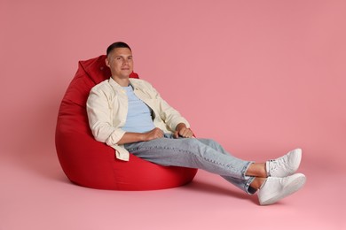 Handsome man on red bean bag chair against pink background