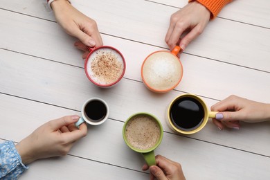 Photo of People holding different cups with aromatic hot coffee at white wooden table, top view