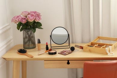 Photo of Mirror, cosmetic products, box of jewelry and vase with pink roses on wooden dressing table in makeup room