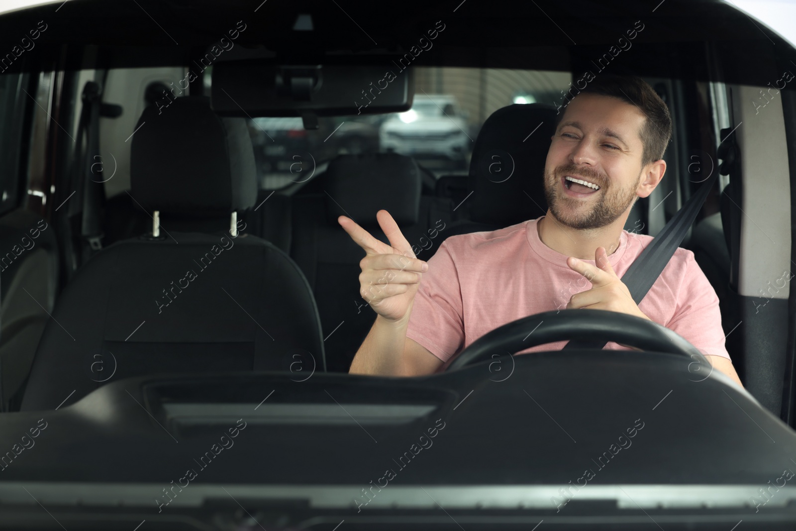 Photo of Listening to radio. Handsome man enjoying music in car, view through windshield