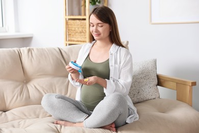 Photo of Beautiful pregnant woman sitting on sofa and taking pills from container at home