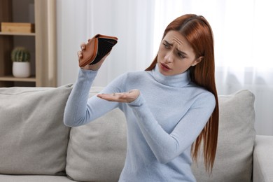Upset woman with empty wallet on sofa indoors