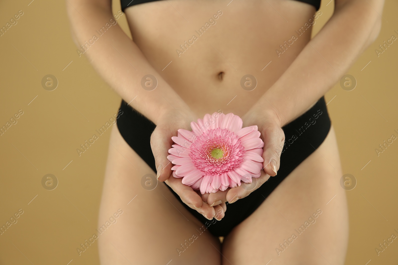 Photo of Gynecology. Woman in underwear with gerbera flower on beige background, closeup