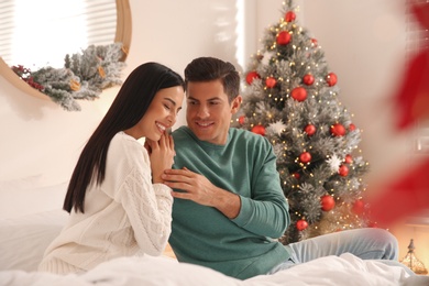 Photo of Happy couple on bed near Christmas tree at home