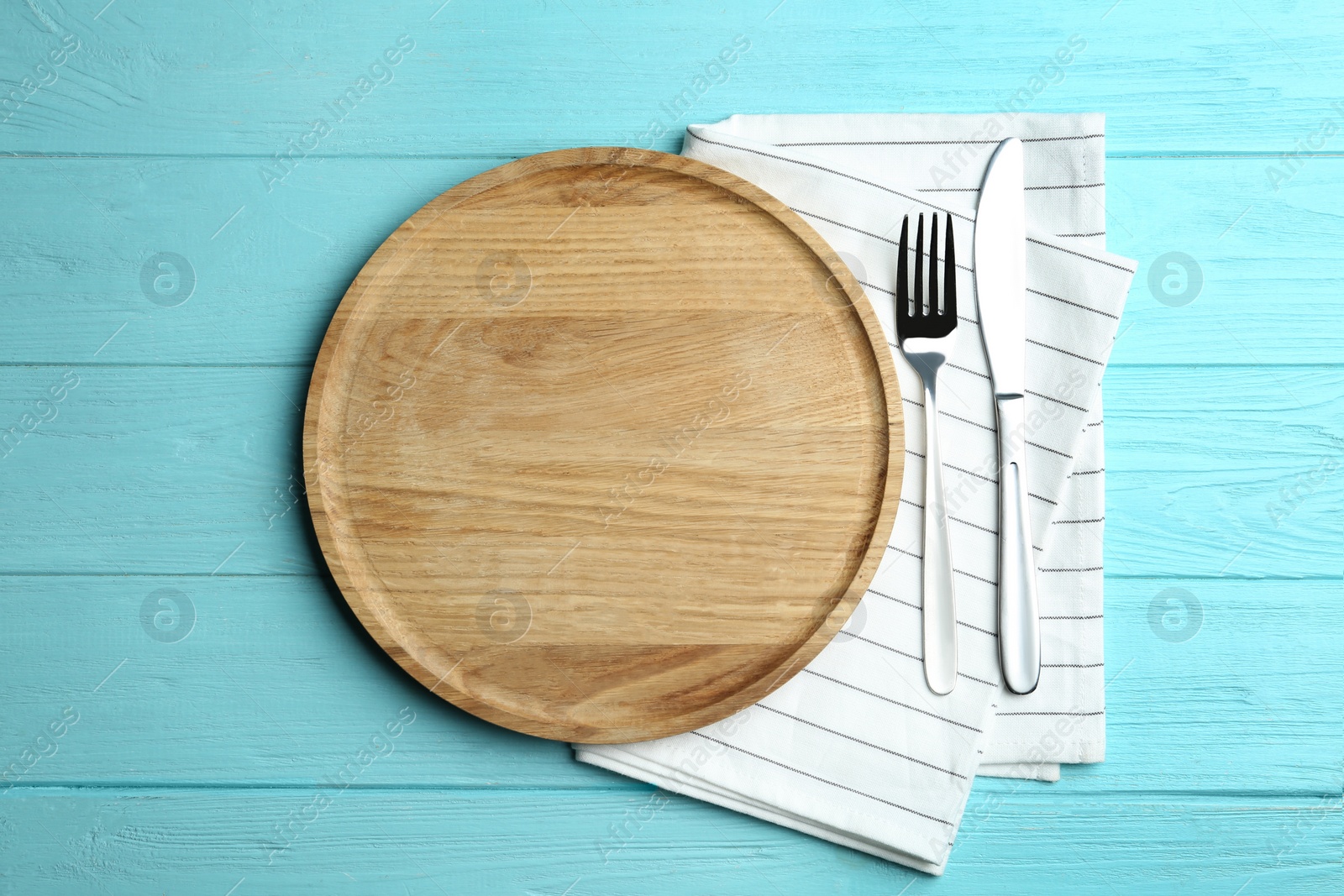 Photo of Wooden plate with cutlery and napkin on light blue table, flat lay