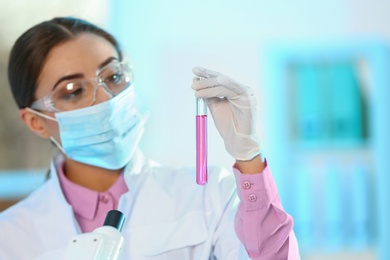 Young scientist holding test tube with sample on blurred background. Laboratory analysis