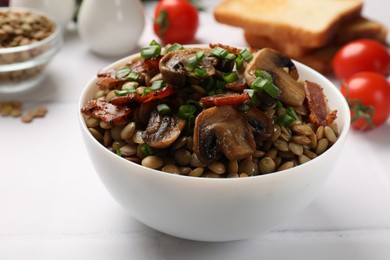 Photo of Delicious lentils with mushrooms, bacon and green onion in bowl served on white table, closeup