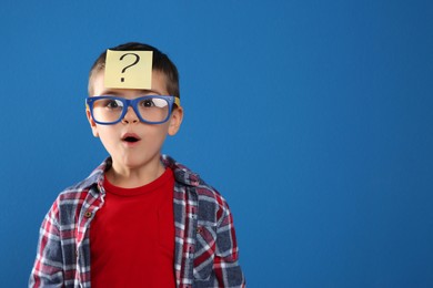Photo of Emotional little boy with question mark on blue background, space for text
