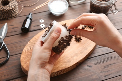 Photo of Woman decorating handmade candle with coffee beans at wooden table, closeup