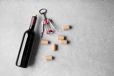 Photo of Wine corks, bottle and corkscrew on light grey table, flat lay. Space for text