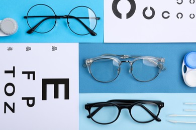 Vision test charts, glasses, lenses and tweezers on light blue background, flat lay