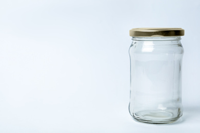 Photo of Closed empty glass jar on light background, space for text