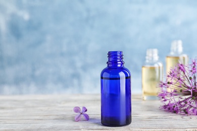 Bottle of essential oil with flowers on wooden table against color background, space for text