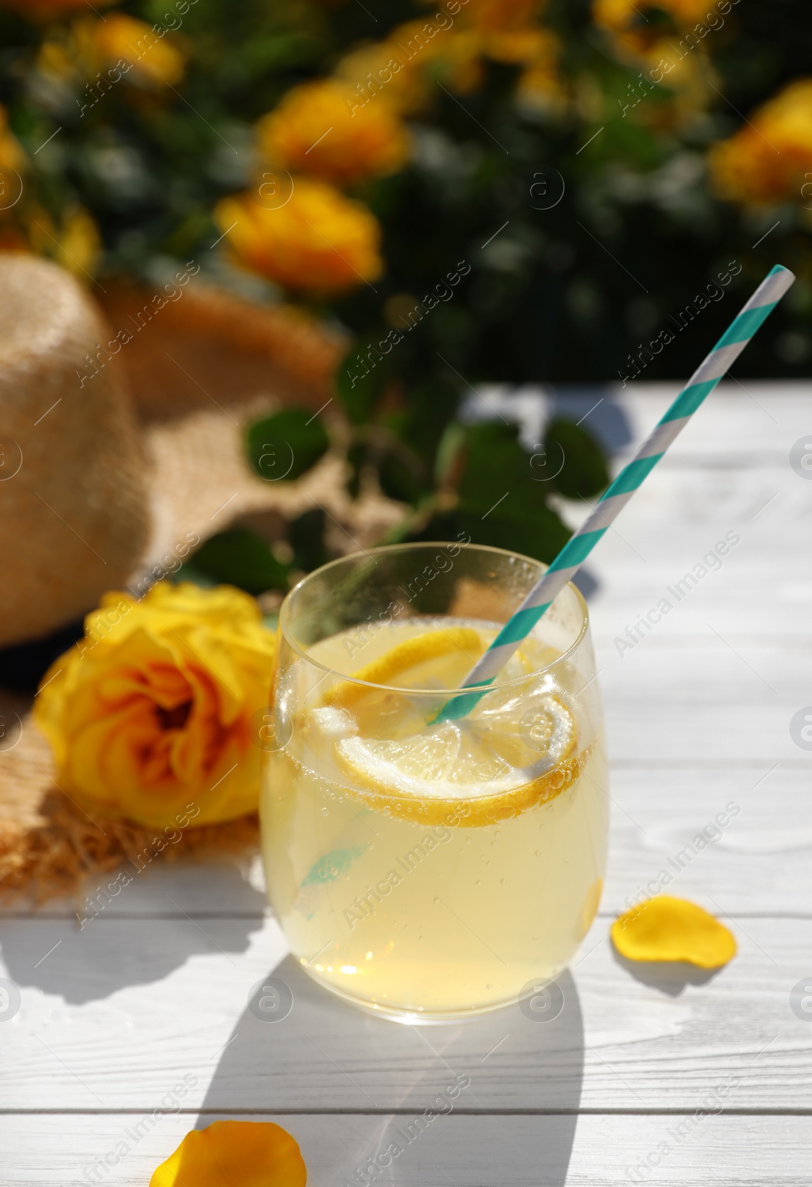 Photo of Composition with glass of refreshing lemonade and beautiful rose on white wooden table in blooming garden