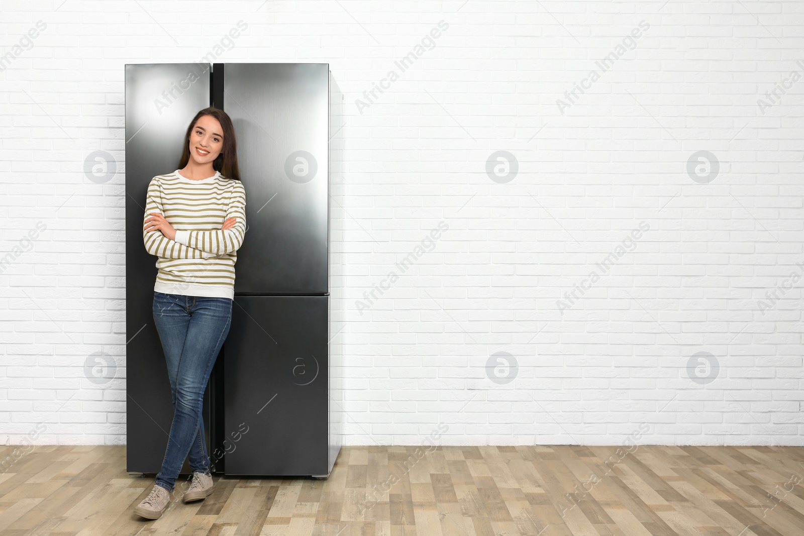 Photo of Happy young woman near refrigerator indoors, space for text