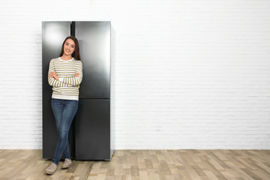 Photo of Happy young woman near refrigerator indoors, space for text