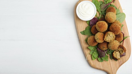 Delicious falafel balls with herbs and sauce on white wooden table, top view. Space for text