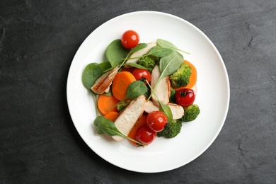 Photo of Delicious salad with chicken, vegetables and spinach  on black table, top view