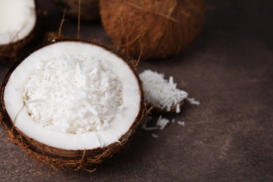 Coconut pieces in nut shell on brown table, space for text