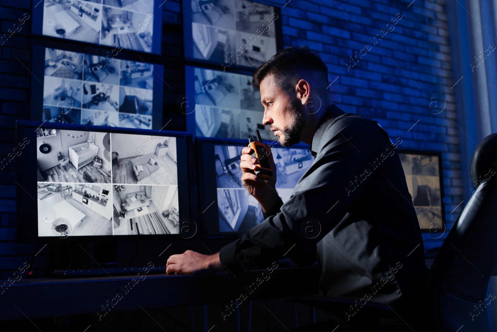 Photo of Male security guard with portable transmitter monitoring modern CCTV cameras indoors