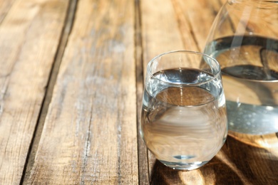 Photo of Glass and jug of water on wooden table, space for text. Refreshing drink