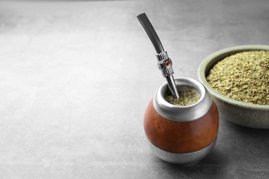 Calabash with bombilla and bowl of mate tea leaves on grey table, space for text